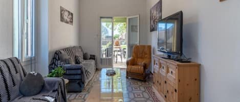 Una sala de estar con sofá, sillón, televisor, aparador de madera y suelo estampado.