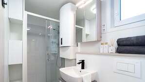 Un baño moderno con cabina de ducha de vidrio, un lavamanos blanco con grifo negro y un espejo sobre el lavamanos.