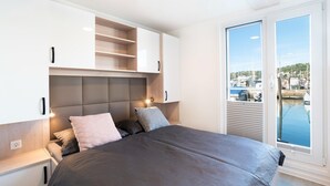Un dormitorio con cama, almacenamiento integrado, mesitas de noche y vistas a un puerto deportivo a través de un ventanal grande.