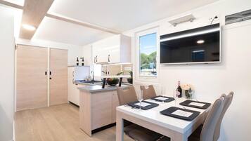 A modern kitchen with a dining area, wooden cabinets, a built-in TV, and a window providing a view of the outdoors.