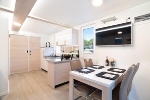 Une cuisine moderne avec un coin repas, des meubles en bois, un téléviseur encastré et une fenêtre donnant sur l’extérieur.