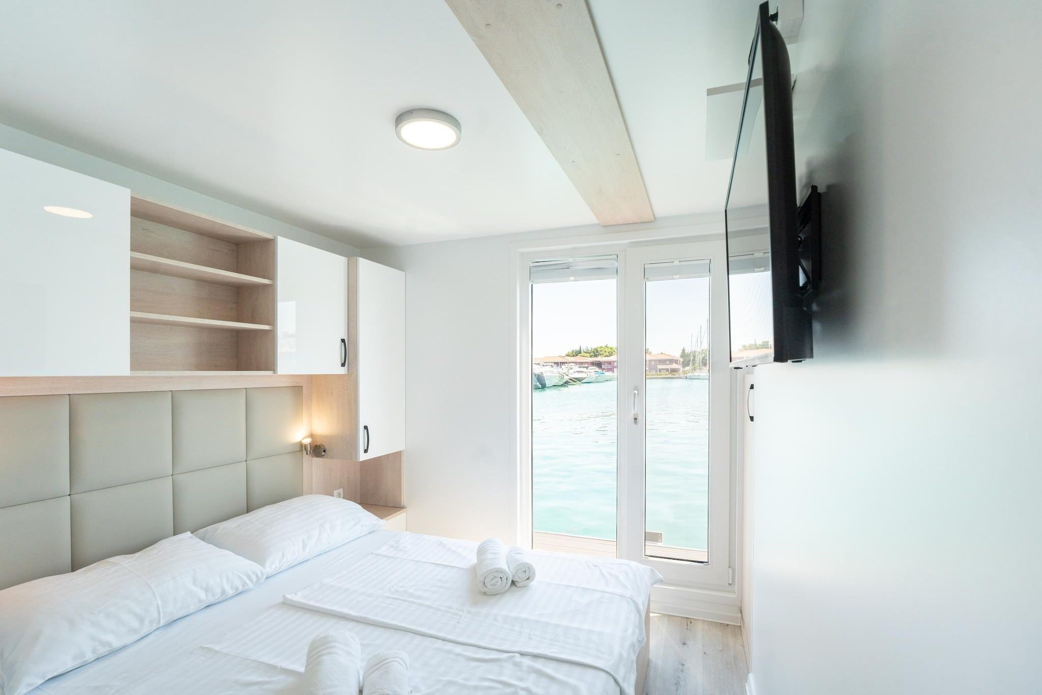 Une chambre d’hôtel avec un lit, un téléviseur fixé au mur et une vue sur la mer par une grande fenêtre.