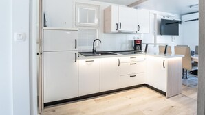 Une cuisine moderne avec des armoires blanches, un robinet noir, une machine à café et un téléviseur à écran plat fixé au-dessus du comptoir.