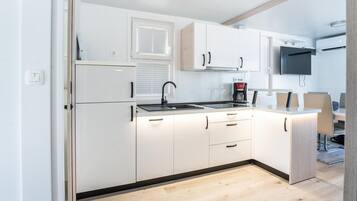 A modern kitchen with white cabinets, a black faucet, a coffee maker, and a flat-screen TV mounted above the counter.