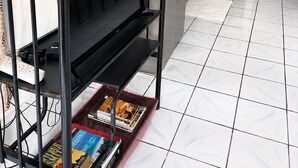 Une cuisine de taille réduite, avec un réfrigérateur noir, un four à micro-ondes et un évier. On y trouve une plante en pot sur le plan de travail et une étagère remplie de livres.