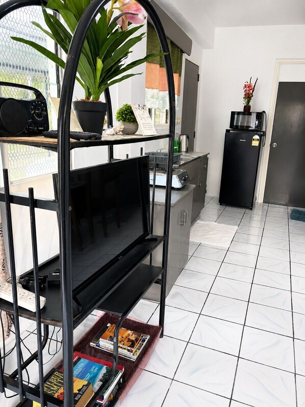 Cocina compacta con un refrigerador negro, un microondas y un lavamanos. Hay una planta en maceta en la encimera y una estantería con libros.