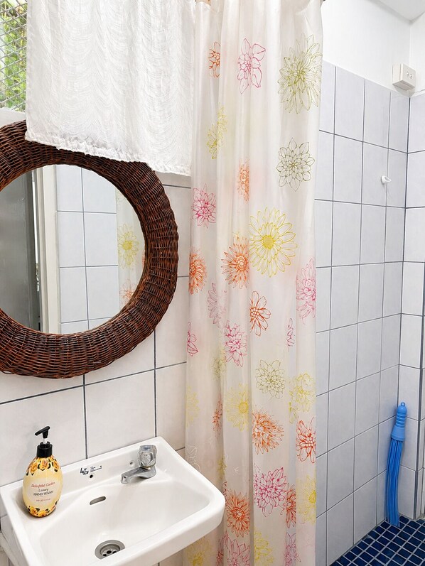 A bathroom with a white sink, a wicker mirror, a floral shower curtain, and a blue-handled brush. - Lovely 4 Bedroom Bountiful Home (Nadi)