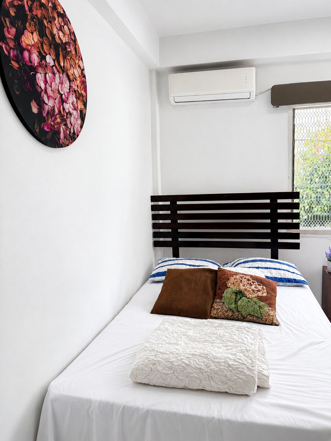 A bedroom with a bed, a wall-mounted air conditioner, and a window with a view.