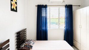Une chambre à coucher comprenant un lit, une table de chevet, une armoire, une fenêtre avec des rideaux et un appareil de climatisation.