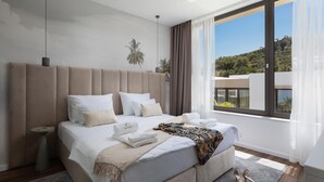 Ett modernt hotellrum med en stor säng, ett nattduksbord, ett fönster med utsikt över landskapet och ett par skor som står på golvet.