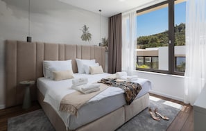 A modern hotel room with a large bed, a nightstand, a window with a view of the landscape, and a pair of shoes on the floor. - Beautiful home in Tkon (Tkon)