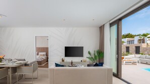 A modern living room with a sofa, a dining area, a TV mounted on the wall, and a view of the outdoor pool area. - Stunning home in Tkon (Tkon)