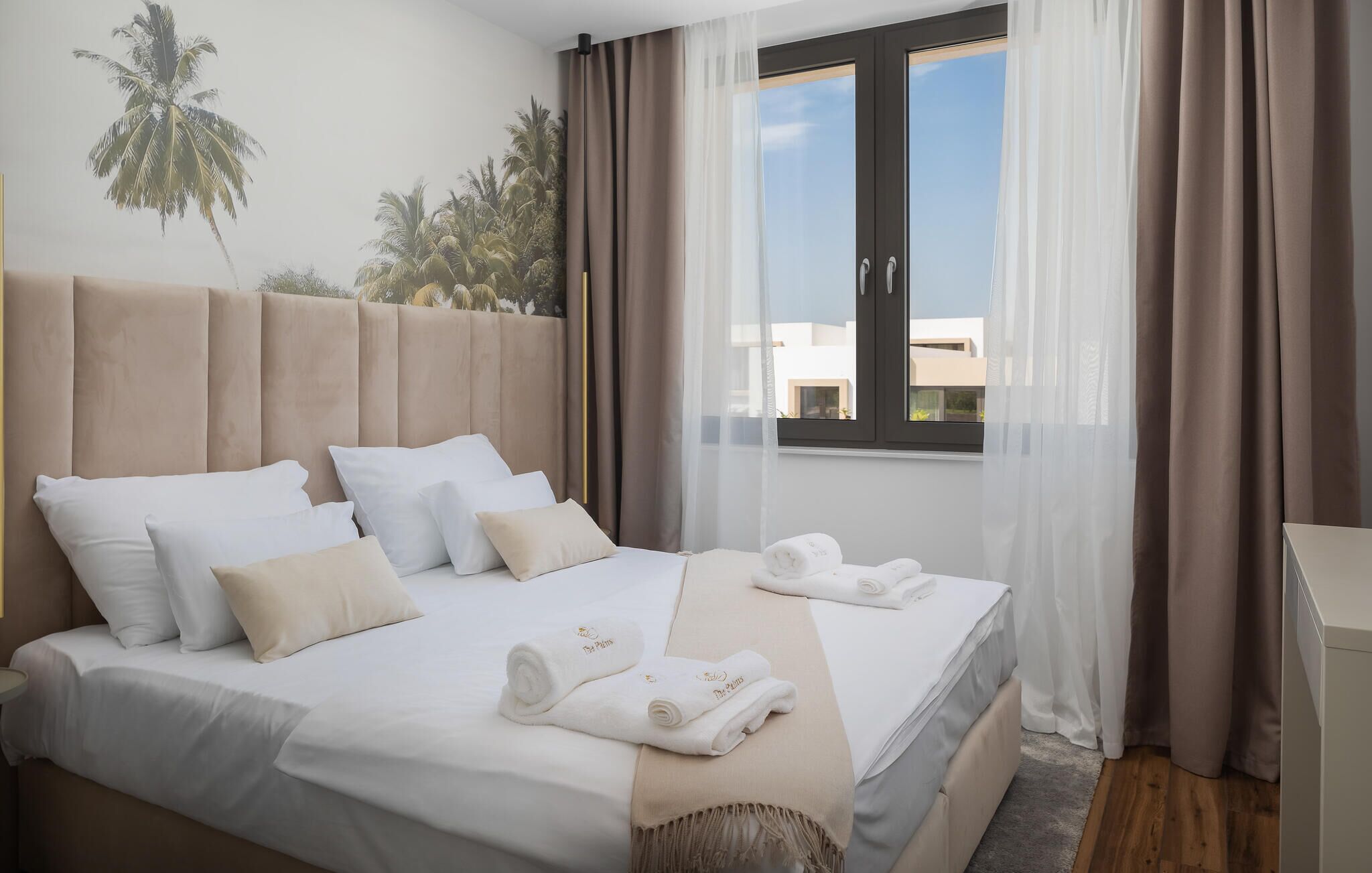 A hotel room with a bed, pillows, a window with curtains, and a wall mural.