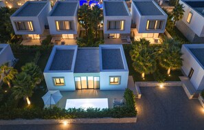 Ein moderner Wohnkomplex mit mehreren freistehenden Häusern, jedes mit Flachdach, großen Fenstern und einem gepflegten Gartenbereich.