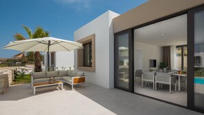 Un espace de vie extérieur moderne comprenant un canapé, une table basse et un parasol, ainsi qu’un coin repas avec des chaises et une table.