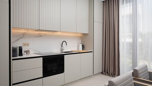 Une cuisine moderne avec des meubles blancs, un lave-vaisselle Bosch noir et une fenêtre ornée de rideaux légers.