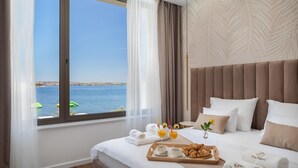 A hotel room with a large window, a bed with white linens, a tray with croissants and coffee, and a view of the sea. - Stunning home in Tkon (Tkon)