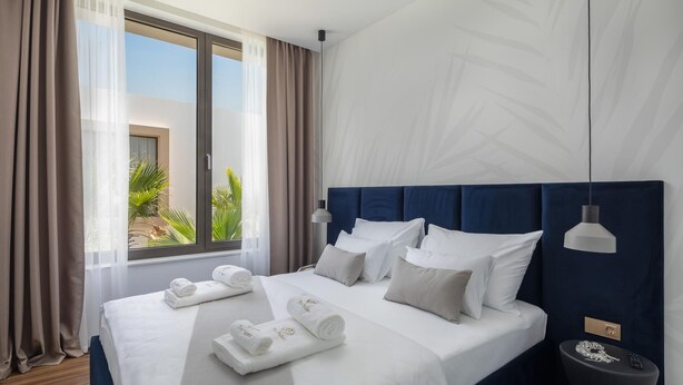 A hotel room with a large bed, a bedside table, a nightstand, a window with curtains, and a view of greenery outside. - Gorgeous home in Tkon (Tkon)