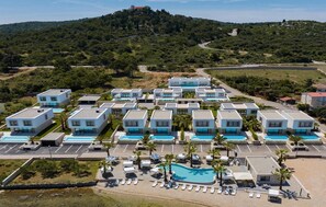 Ein Resort mit modernen Gebäuden, einem zentralen Schwimmbecken und einer Bergkulisse.