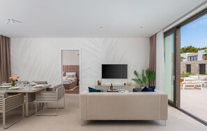 Ein modernes Wohnzimmer mit Essbereich, einem an der Wand befestigten Flachbildfernseher und einem großen Fenster mit Blick nach außen.