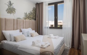 Ein Hotelzimmer mit Bett, Kissen, einem Fenster mit Vorhängen und einem Handtuch mit Logo.