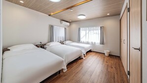 A hotel room with three beds, wooden flooring, a ceiling light, and an air conditioning unit. - house tabiji nishikujyo (Nishikujo, Konohana Ward)