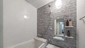 A modern bathroom with a bathtub, a shower, and a vanity with a mirror and shelves for toiletries. - house tabiji nishikujyo (Nishikujo, Konohana Ward)