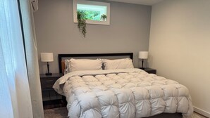 Quarto com uma cama, duas mesas de cabeceira, uma janela com uma planta e piso coberto de carpete.
