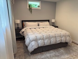 Ein Schlafzimmer mit einem Bett, zwei Nachttischen, einem Fenster mit Pflanze und Teppichboden.