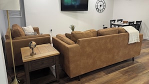 Uma sala de estar moderna com um sofá marrom, uma mesa de centro de madeira, um globo e uma TV na parede.