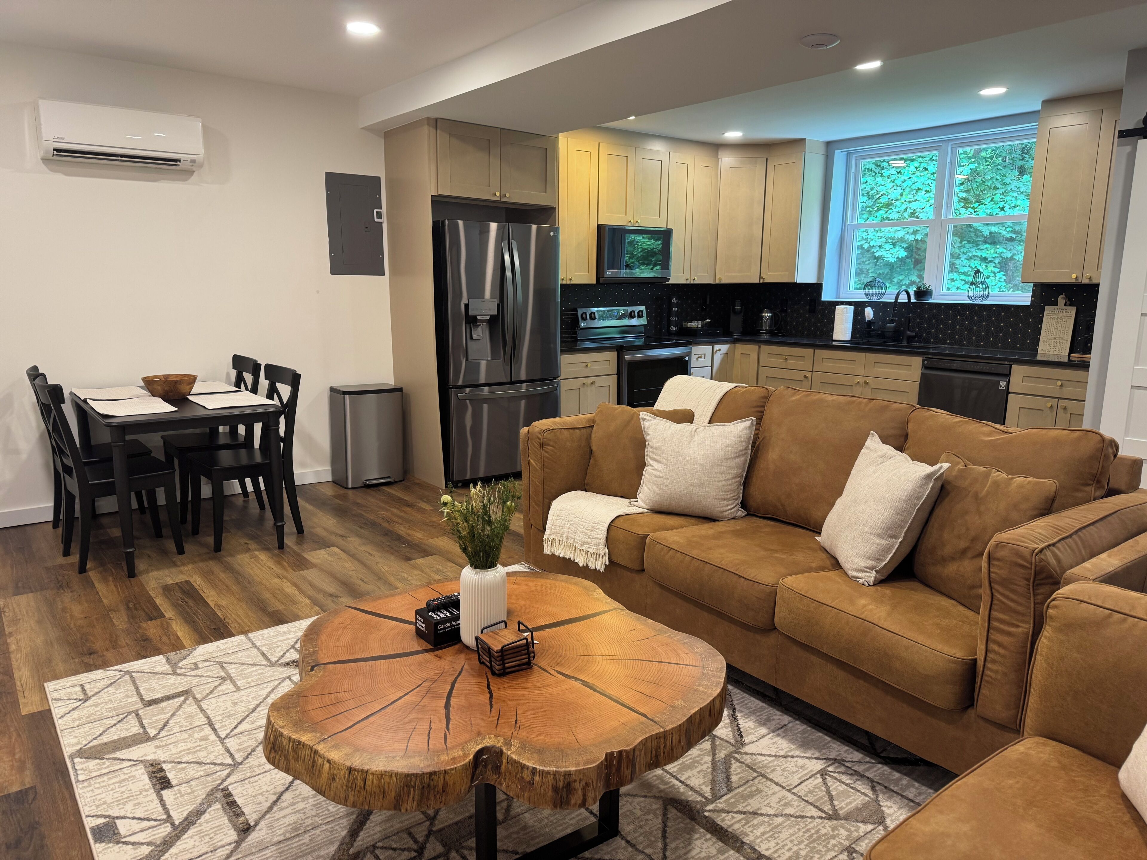 Un salon moderne avec un canapé marron, une table basse en bois et un coin repas comprenant une table et des chaises noires.
