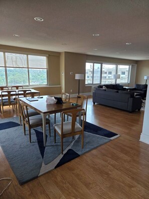 Un amplio salón con una mesa de comedor, sillas, un sofá y un ventanal que ofrece vistas de la ciudad.