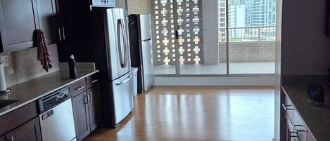A modern kitchen with dark cabinets, stainless appliances, and a large window overlooking a cityscape.