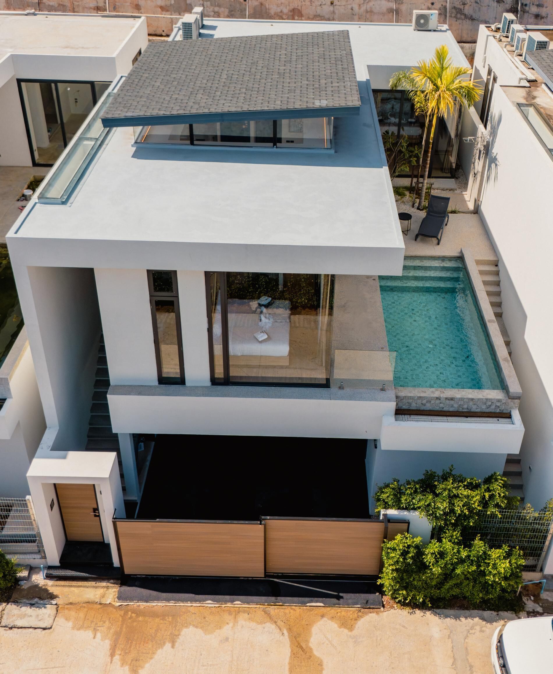 Een modern huis met twee verdiepingen, een dakterras, een zwembad en een garage.
