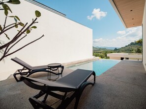 A modern outdoor pool area with lounge chairs and a table, surrounded by a white wall and a view of a mountainous landscape. - Villa Kauri 3BR at Aileen Naithon (Sa Khu)