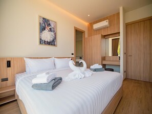 A hotel room with a large bed, a painting on the wall, a mirror, and an air conditioning unit. - Villa Kauri 3BR at Aileen Naithon (Sa Khu)