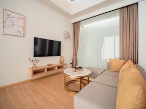 A modern living room with a flat-screen TV, a round coffee table, a sofa, and a sliding glass door with curtains. - Villa Kauri 3BR at Aileen Naithon (Sa Khu)