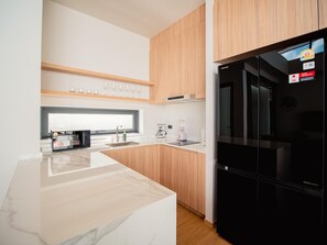 A modern kitchen with a black refrigerator, wooden cabinets, a marble countertop, and a coffee machine. - Villa Kauri 3BR at Aileen Naithon (Sa Khu)