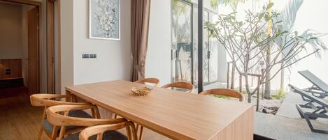 A modern dining area with a wooden table and chairs, a painting on the wall, and a view of the outdoors.