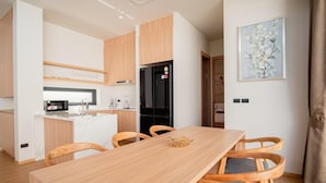 A modern kitchen with wooden cabinets, a black refrigerator, and a dining area with a wooden table and four chairs. - Villa Kauri 3BR at Aileen Naithon (Sa Khu)