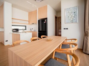 A modern kitchen with wooden cabinets, a black refrigerator, and a dining area with a wooden table and four chairs. - Villa Kauri 3BR at Aileen Naithon (Sa Khu)