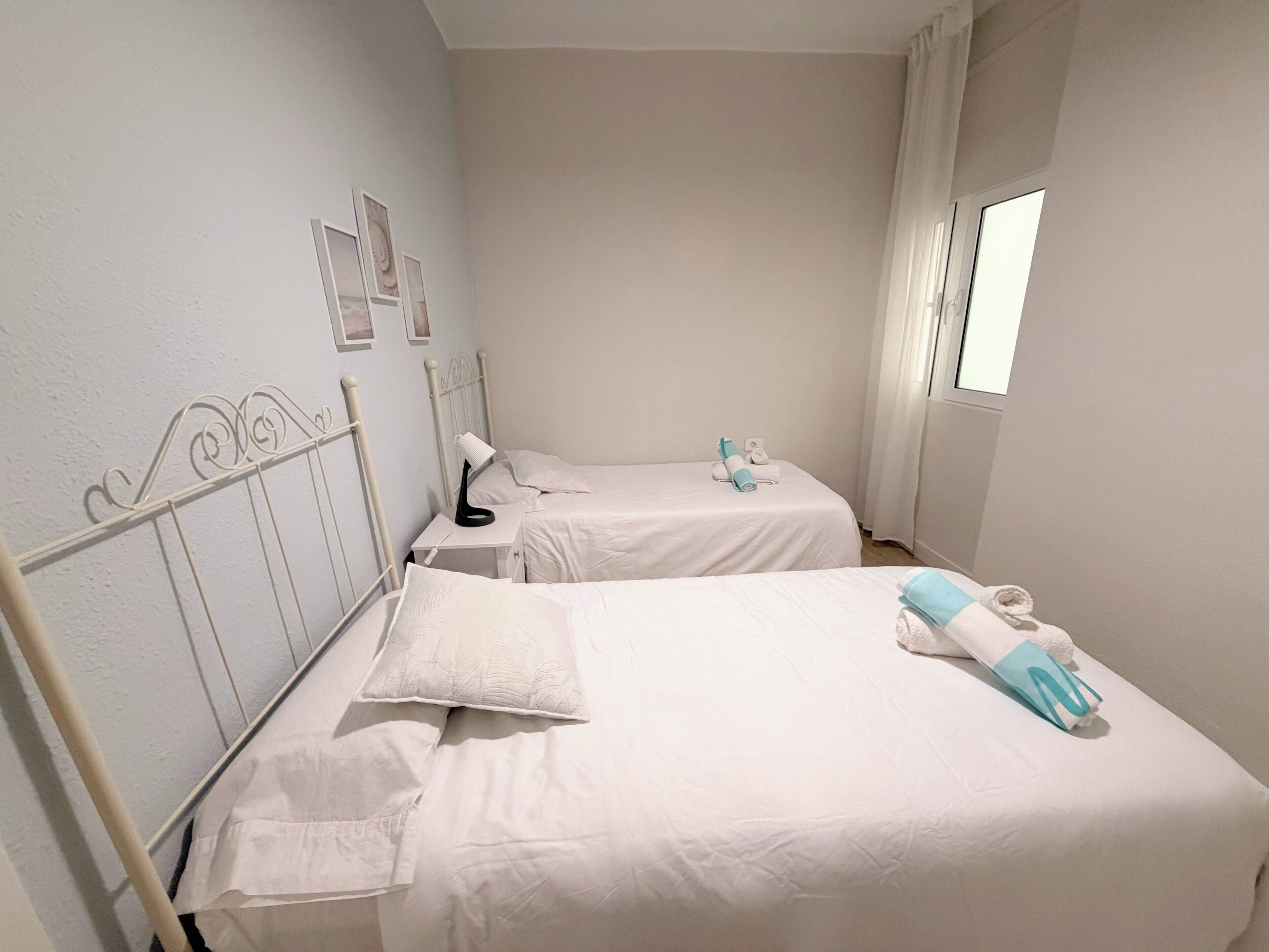 Habitación de hotel con dos camas, un escritorio, una lámpara y un ventanal con cortinas.