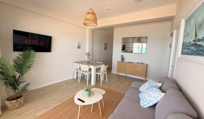 A modern living room with a flat-screen TV, a dining area, a sofa, and a large plant. - La Palmera - Amazing beachfront terrace (Cullera)