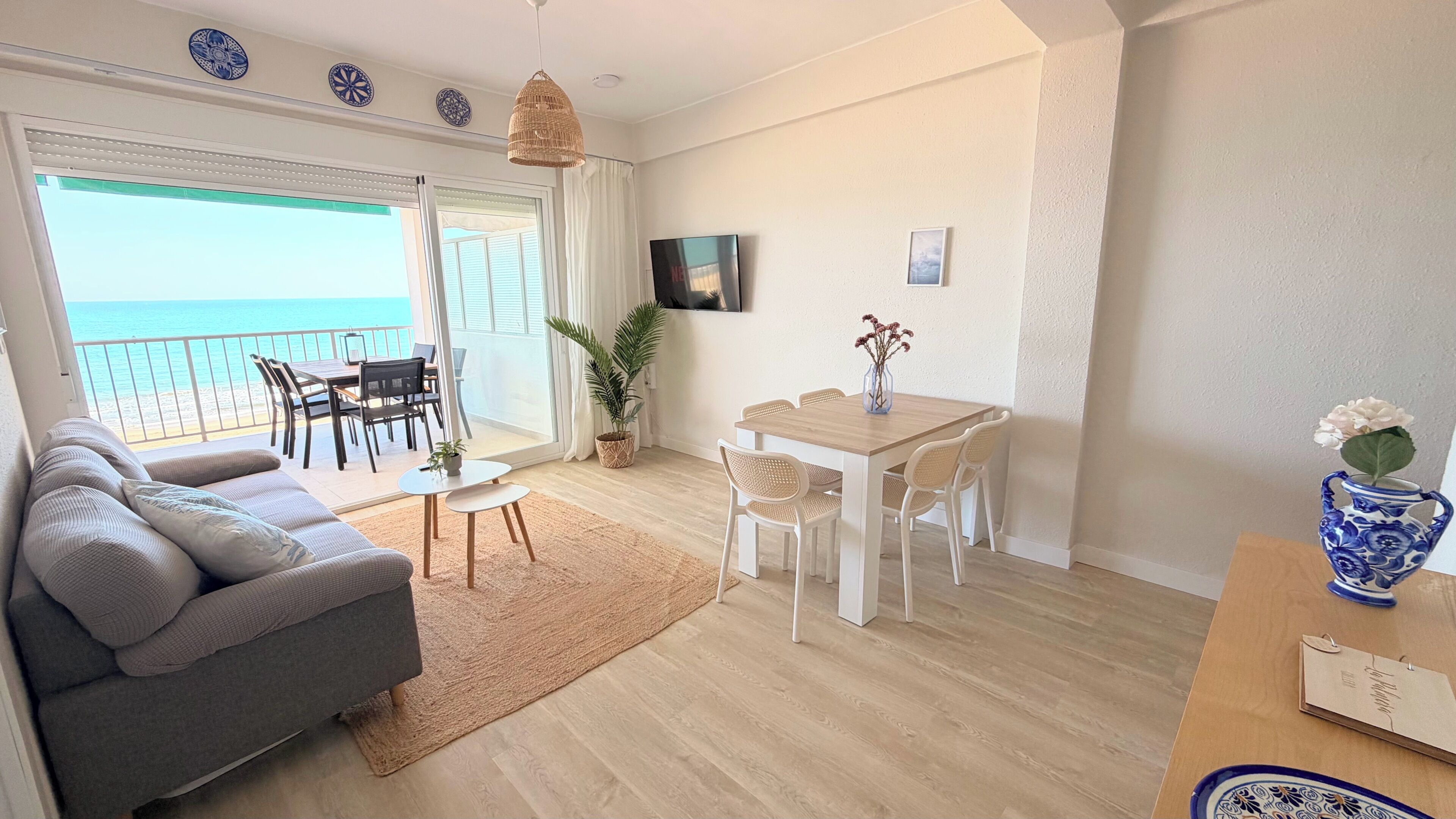 A living room with a sofa, dining table, chairs, a TV, and a view of the sea.