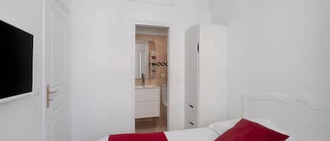 Habitación de hotel con cama, televisión, armario y baño visible a través de una puerta abierta.