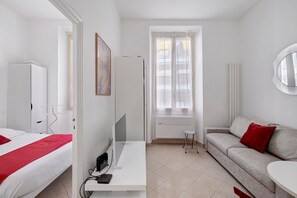 Ett hotellrum med en säng, ett skrivbord med en dator, en soffa och ett fönster med gardiner.