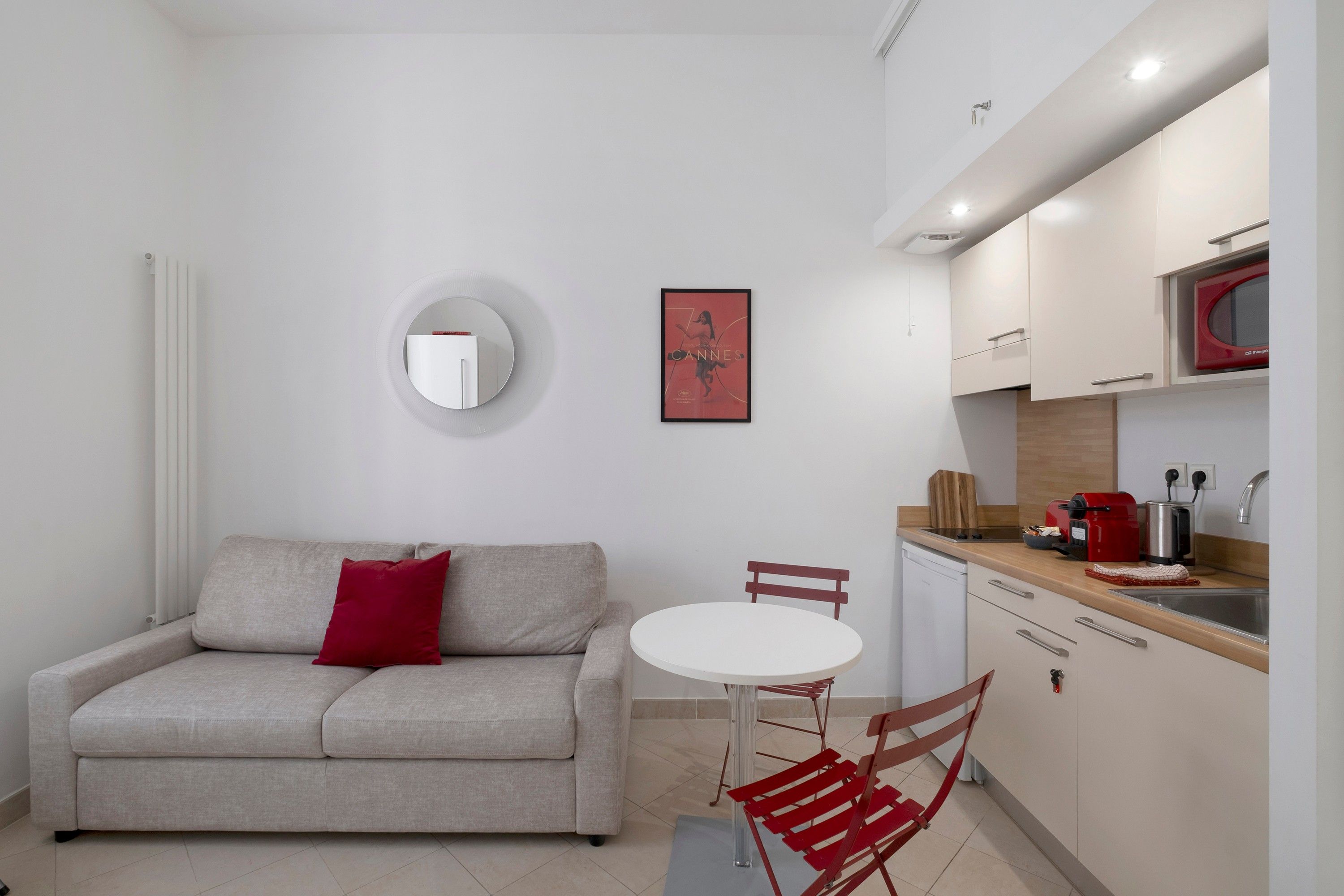 A compact living space with a sofa, a round mirror, a small table, and a kitchenette.