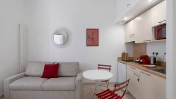 A compact living space with a sofa, a round mirror, a small table, and a kitchenette.