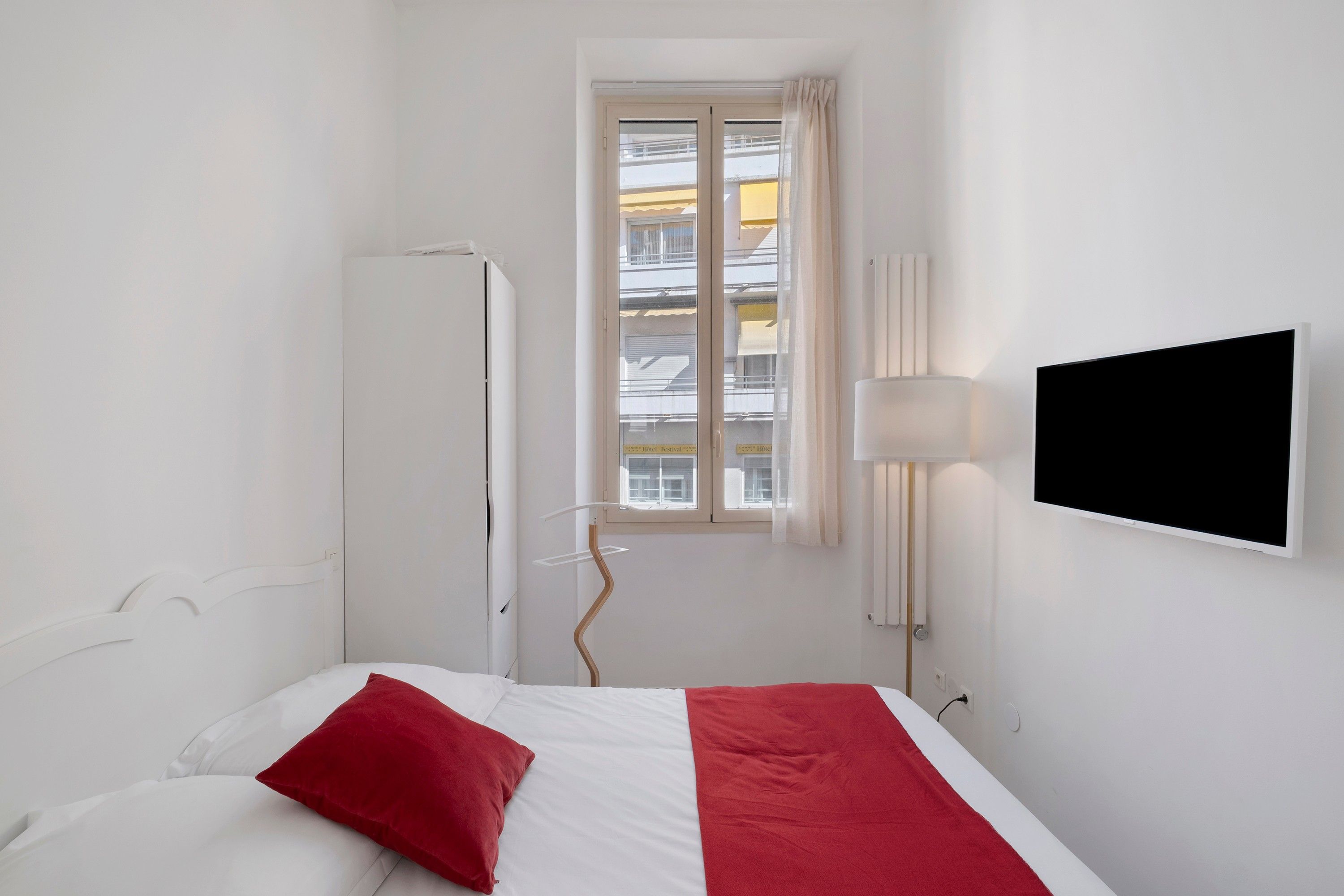 A hotel room with a bed, a TV, a window, and a radiator.