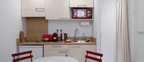 A compact kitchen with a microwave, toaster, kettle, and sink. There is a round table with two chairs.